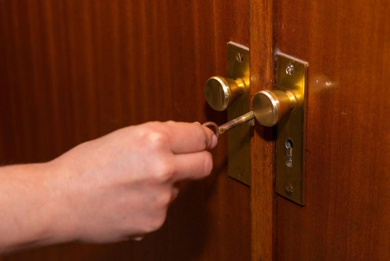 Hand turning a brass key in a wooden door, illustrating spare keys kept in a safe